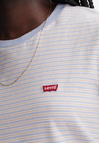 Blå och vit randig t-shirt med en ljusgul rand, med en röd Levi's logotypapplikation på bröstet och rund halsringning.