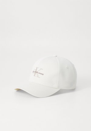 White baseball cap made of cotton blend fabric, featuring an embroidered logo in light brown. Curved brim with textured surface.