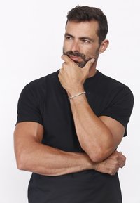 Black short-sleeve t-shirt, muscular arms crossed. Silver bracelet on wrist, medium length hair, light facial hair, neutral background.