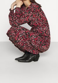 Robe fleurie noire avec des fleurs roses et blanches, ourlet à volants, manches longues, associée à des bottines noires à talon bloc.