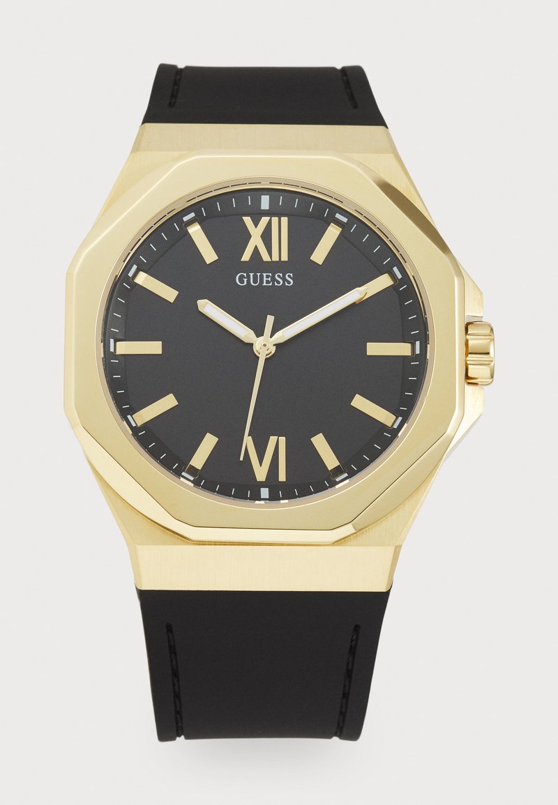 Relógio com mostrador preto, marcadores de horas em ouro bold e numerais romanos. Apresenta uma luneta octogonal em ouro e uma pulseira de borracha preta.