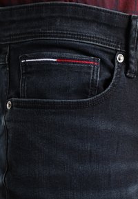 Ciemnoniebieskie dżinsy z przednią kieszenią, ozdobioną paskowym akcentem w kolorach czerwonym, białym i niebieskim oraz srebrnym guzikiem z logo.