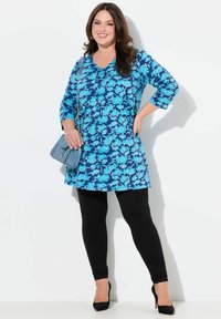 Blå blommig tunika med trekvartsärmar, i kombination med svarta leggings och högklackade skor, accentuerad av en liten blå handväska.