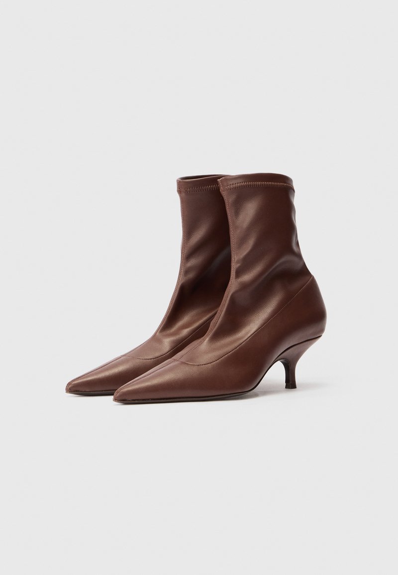 Ett par bruna läderstövlar med spetsig tå och låg kittenklack samt släta stretchmaterial på ovandelen mot en ren vit bakgrund.