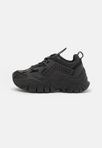 Scarpe da ginnastica nere con suola spessa, parte superiore in sintetico liscio, dettagli perforati e punta arrotondata. Presentano una chiusura con lacci e un'etichetta per il trasporto.