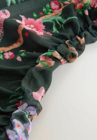 Grüner floraler Netzstoff mit rüschensäumigen Kanten, der rosa und lila Blumen auf einem dunklen Hintergrund zeigt. Strukturierte und leichte Ausführung.