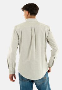 Camicetta a maniche lunghe a righe in verde chiaro e bianco, con colletto button-down e orlo curvato. Il tessuto ha una texture liscia, adatta per l'abbigliamento casual.