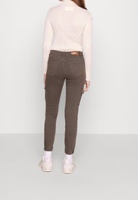 Pantaloni cargo marroni con tasche laterali, gambe affusolate e una maglietta a maniche lunghe ribbed rosa chiaro. Presenta un'etichetta con il logo sulla parte posteriore della vita.