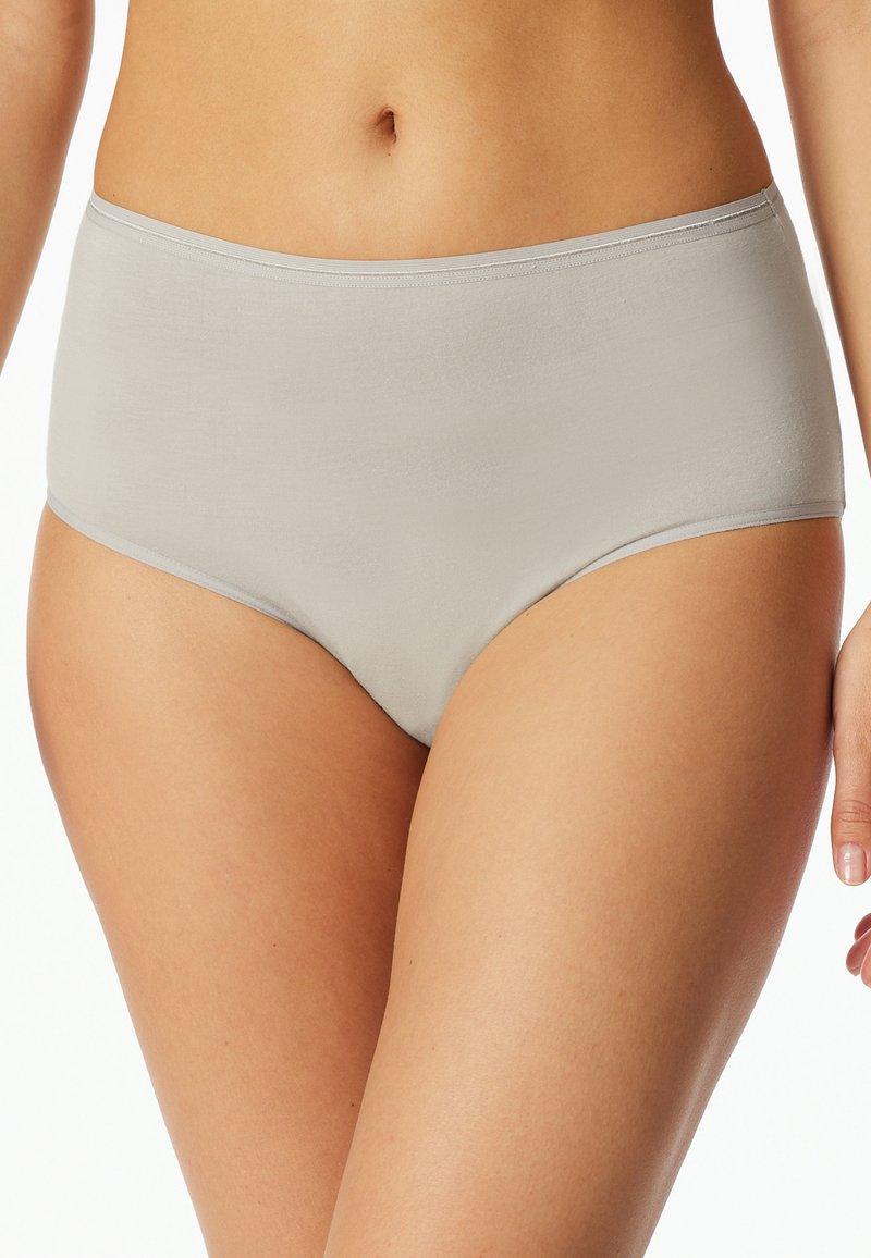 Kobieta nosząca jasnoszare bawełniane majtki o wysokiej talii, pokazująca tors od talii do połowy uda na białym tle.