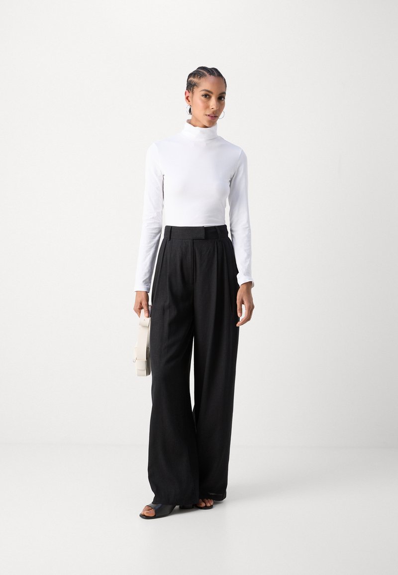 Maglia bianca a maniche lunghe con collo a polo abbinata a pantaloni neri a gamba larga. Il top ha una texture liscia, mentre i pantaloni presentano un design strutturato.