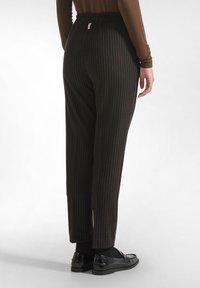 Pantalones oscuros de rayas con un tejido ligero. Tienen una cinturilla elástica y piernas ajustadas. Combinados con mocasines de charol negros.