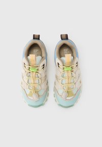 Ζευγάρι παιδικά αθλητικά παπούτσια σε μπεζ και μπ λε χρώμα με πράσινες κορδόνια με κούμπωμα, σε λευκό φόντο, φωτογραφημένα από ψηλά.