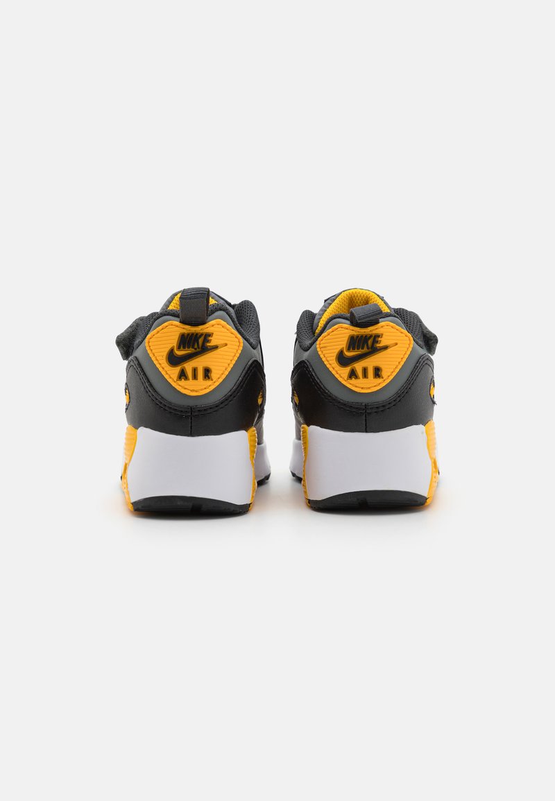 Zapatillas Nike Air en negro y amarillo con parte trasera texturizada, suelas blancas y un logotipo prominente. Presenta un collar acolchado y parte superior de malla.