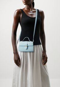 Světle modrá kožená kabelka se strukturovaným tvarem, horní rukojetí a odnímatelným ramenním popruhem. Obsahuje přední klopu a zlaté kování.