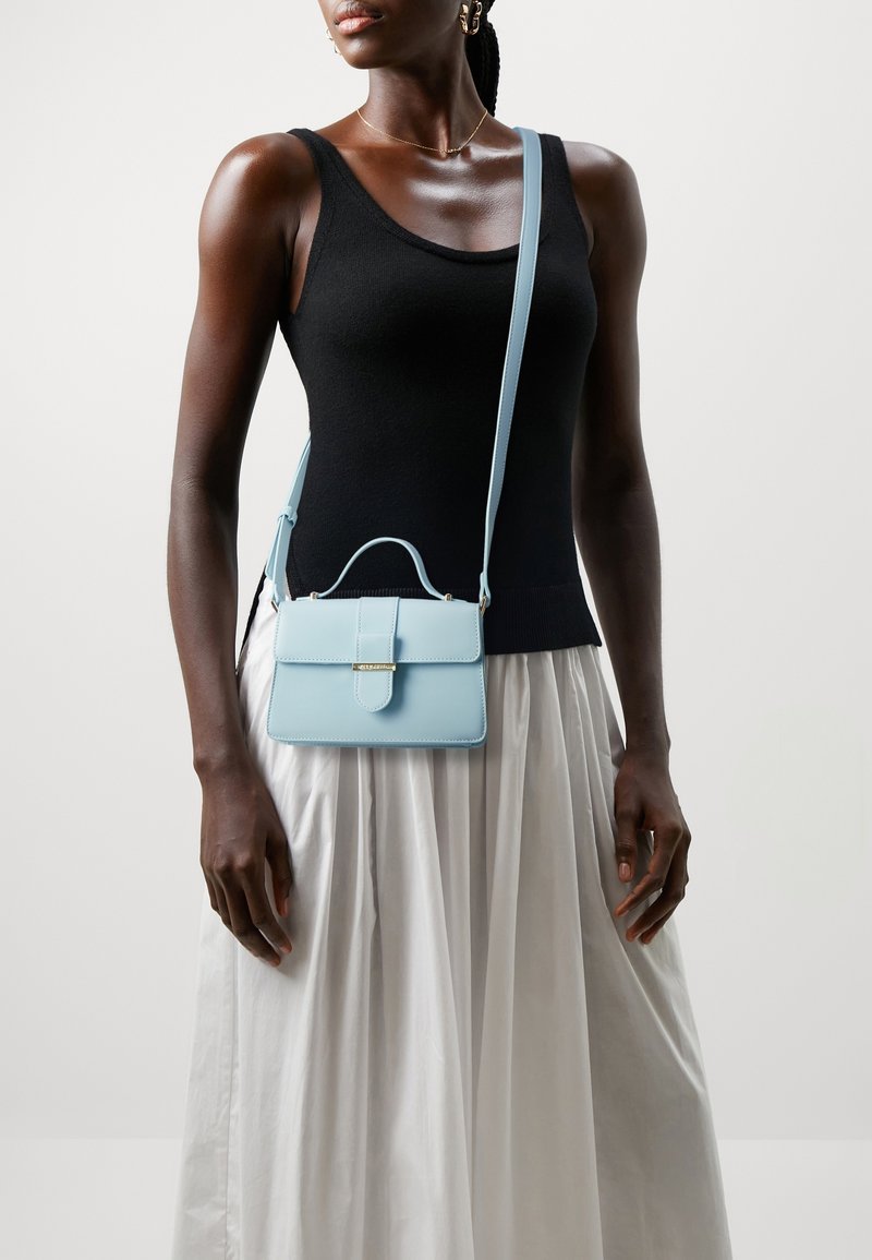 Světle modrá kožená kabelka se strukturovaným tvarem, horní rukojetí a odnímatelným ramenním popruhem. Obsahuje přední klopu a zlaté kování.