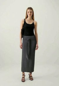 Top din dantelă neagră, fustă maxi gri cu detalii de legare la talie și sandale negre cu bretele. Design simplu, material ușor și culori neutre.