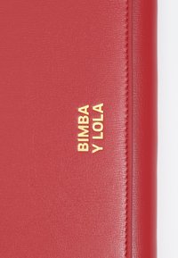 Czerwony dokumentownik z imitacji skóry, ozdobiony złotym wytłoczonym napisem "BIMBA Y LOLA" oraz szczegółowym przeszyciem na krawędzi.