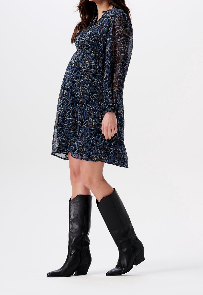 Kleid mit maritimen Muster und langen, transparenten Ärmeln, geraffter Taille und einem über dem Knie endenden Saum, kombiniert mit schwarzen, ledernen Stiefeln bis zum Knie.
