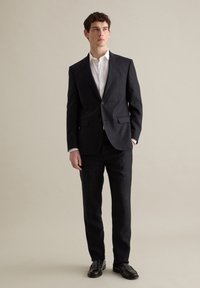 Traje navy hecho de tela texturizada, con cierre de un solo botón, dos bolsillos frontales y pantalones a juego, combinado con una camisa blanca.