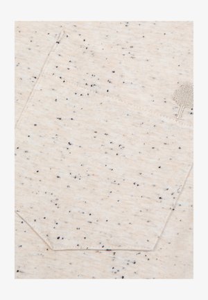 Close-up van beige gevlekt stof met een gestikte zak en een klein geborduurd boompje-detail aan de rechterzijde.