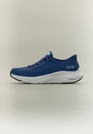 Μπλε αθλητικό παπούτσι Skechers Slip-Ins με λευκή ανάγλυφη αφρώδη σόλα και σχέδιο με κορδόνια σε απλό μπεζ φόντο.