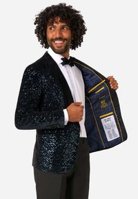 Námorníkový blejzer so štrassovými detailmi a čiernymi zamatovými klopami, úzky strih. Interiér obsahuje podšívku s modrým vzorom a viaceré vrecká s textovým detailom.