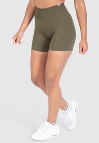 Olijf groene high-waisted shorts gemaakt van rekbaar materiaal. Gladde textuur, met een getailleerd ontwerp en een label op de tailleband. Gepaard met witte sneakers.