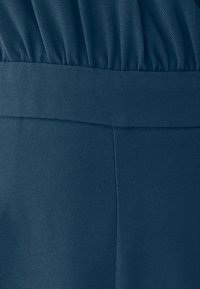 Tumedast nailonist elastne vöökoht, millel on sile tekstuur ja diagonaalne ribane muster, selgelt nähtavad korralikud õmblused ja saated.