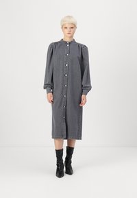 Grå denimkjole med lange puffermer, knappelukking og samlet mansjett, kombinert med svarte spisse knelang støvler.
