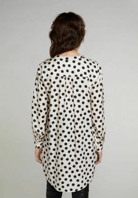 Blusa a maniche lunghe color crema con grandi pois neri. Presenta una chiusura con bottoni sul retro, orlo arrotondato e dettagli arricciati sulle spalle.