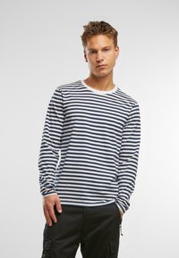 Hosszú ujjú, csíkos ing sötétkék és fehér színben, kör neckline-nel és illeszkedő mandzsettákkal. Az anyag sima textúrájú és laza illeszkedésű.
