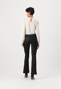 Blusa beige chiaro con apertura a chiave sul retro, maniche a sbuffo; abbinata a pantaloni flared neri in ecopelle e stivaletti con tacco alto.