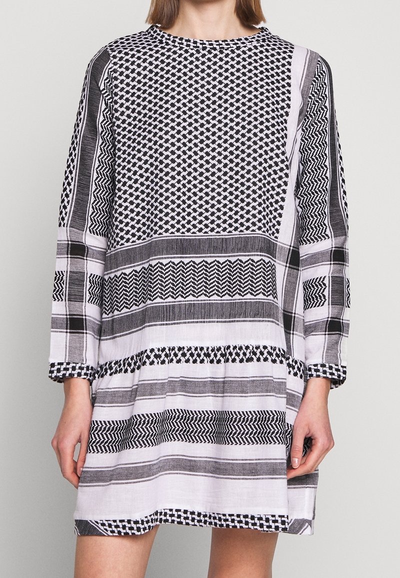 Vestido de manga larga en blanco y negro. Presenta patrones geométricos, variaciones en el grosor de las rayas y un corte relajado con un dobladillo fruncido.