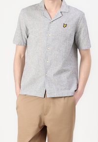 Kurzärmeliges, hellgraues Hemd mit Knöpfen aus strukturiertem Stoff, mit einem gelben Schmetterlingslogo auf der linken Brust und einem Reverskragen.