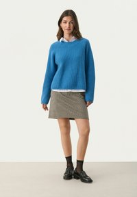 Blå ribbet sweater med lange ærmer, lagd over en hvid skjorte; parret med en ternet mini nederdel og sorte loafers med ankelstrømper.