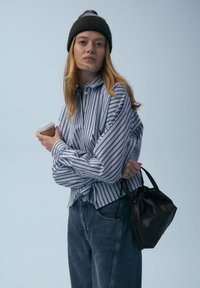Chemise rayée bleu et blanc avec boutons, coupe décontractée, associée à un jean taille haute bleu clair et un sac à main noir à cordon. Tasse de café à la main.