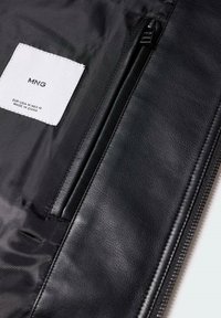 Interno di una borsa in pelle nera che presenta un'etichetta bianca con logo, una texture in tessuto e una tasca con zip lungo un lato.