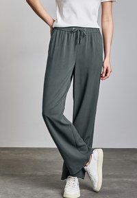Pantalons gris, légers, à taille élastique avec une coupe décontractée, dotés d'une fermeture à cordon et d'une texture lisse, associés à des baskets blanches.