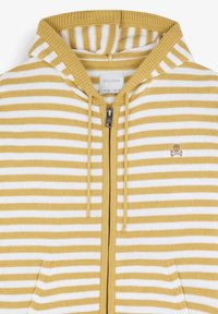 Hoodie zippé à rayures jaunes et blanches avec capuche, poches avant et un petit logo de crâne sur la poitrine gauche. Matière en tricot douce.