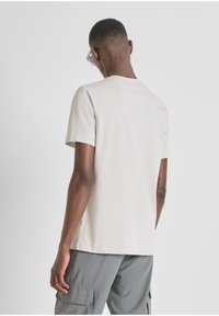 Camiseta corta de manga corta en un color beige claro, fabricada en una tela suave, que presenta un corte relajado y un cuello redondo clásico. Se lleva con pantalones cortos cargo grises.