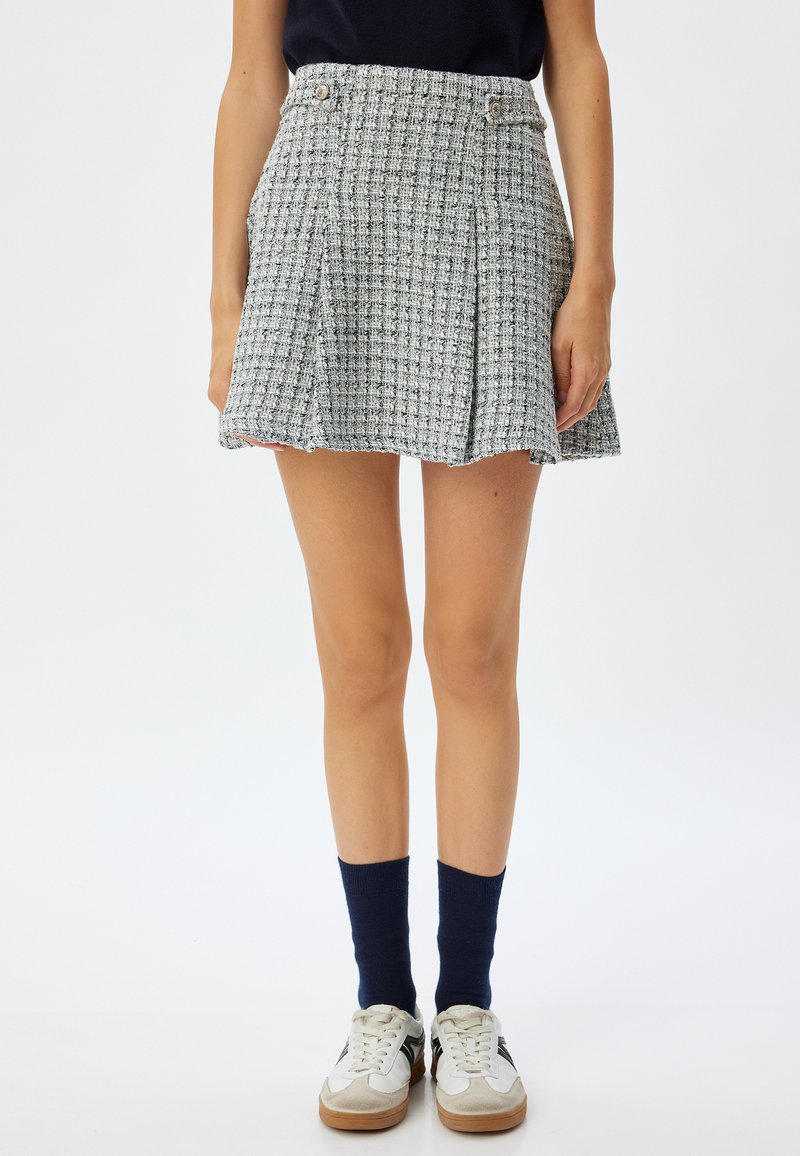Tweed mini nederdel i grå med et ternet mønster, plisseringer foran og to frontknapper. Kombineret med hvide sneakers og marineblå sokker.