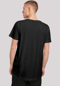 Svart t-skjorte med korte ermer, rund hals og lengre bakkant, laget av mykt bomullsstoff, med et enkelt design.