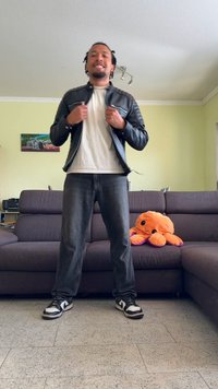 Black leather jacket with quilted accents, white T-shirt, gray jeans, and black and white sneakers. Plush orange octopus on couch.