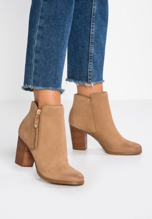 Tan suede ankle boots with a block heel and side zipper detail. The heel features a stacked design, adding texture and contrast.