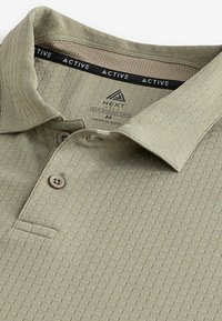 Hellgrünes Poloshirt aus strukturiertem Stoff mit einem subtilen Muster, zwei braunen Knöpfen und einem Netzkragenfutter.