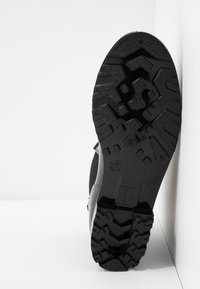 Semelle en caoutchouc noire d'une botte avec des crampons profonds multidirectionnels, taille 37 indiquée, sur fond blanc.