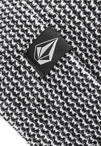 Bonnet en tricot noir et blanc avec un motif texturé et une étiquette noire portant un logo géométrique blanc.