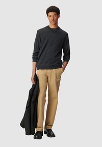 Donkergrijs shirt met lange mouwen, beige broek, zwarte schoenen, houdt een zwarte jas vast. Casual pasvorm met een ronde hals en gestructureerde stof.