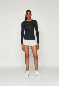 Must valgete logoga must pikkade varrukatega sporditopp, millele on kokku sobitatud valged lühikesed püksid ja valged nikingud mustade detailidega. Sile ja keha järgi lõigatud disain.