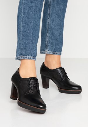 Czarne buty na obcasie z gładkiej skóry z teksturowanym wykończeniem, z ozdobnymi sznurówkami, słupkowym obcasem i brązowymi akcentami przy podeszwie.